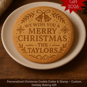 May include: A round, baked cookie with the words "WE WISH YOU A MERRY CHRISTMAS THE TAYLORS" engraved on its surface. The cookie is on a white plate, with a red star-shaped sticker that says "best Gift 2026".