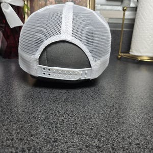 Op de afbeelding: Witte truckerpet met een mesh achterkant en verstelbare druksluiting. De pet heeft een wit voorpaneel en een gebogen klep. De achterkant is van wit mesh voor ventilatie. Geschikt voor casual wear.