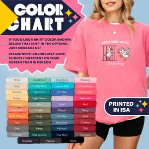 May include: A pink t-shirt with the text "FROM REBEL WINGS" and a graphic of two geese. Below is a color chart with various shirt colors, including white, blue, and black. The text "PRINTED IN ISA" is also visible.