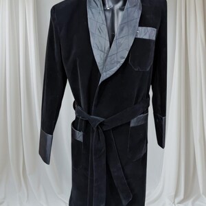 May include: A black velvet robe with a shawl collar and a matching belt. The collar and cuffs have a contrasting gray quilted satin. The robe has two front pockets and a tie closure. The robe is displayed on a mannequin.