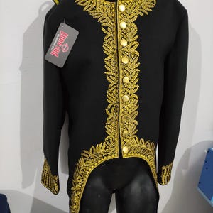 May include: Black jacket with gold embroidery and buttons. The jacket has a high collar and long sleeves. The gold embroidery is intricate and detailed, with a floral pattern. The jacket has a tailcoat design.