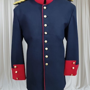 May include: A navy blue military-style jacket with red trim and accents. The jacket features a high red collar, gold buttons, and gold epaulettes. The cuffs are red with gold buttons. The jacket is displayed on a mannequin.