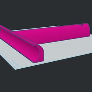 Puede incluir: Un objeto en forma de T de color magenta brillante con un borde frontal curvado y una base plana. El objeto presenta una superficie lisa y s&oacute;lida con un dise&ntilde;o geom&eacute;trico distintivo, colocado sobre una superficie cuadriculada clara.