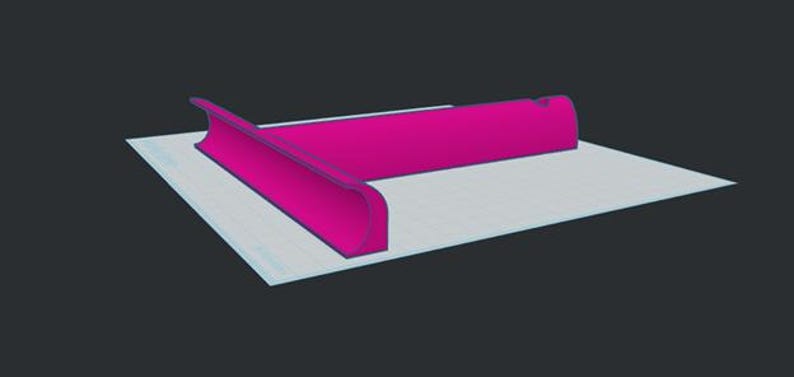Puede incluir: Un objeto en forma de T de color magenta brillante con un borde frontal curvado y una base plana. El objeto presenta una superficie lisa y s&oacute;lida con un dise&ntilde;o geom&eacute;trico distintivo, colocado sobre una superficie cuadriculada clara.