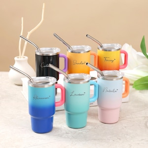 May include: Six colorful insulated tumblers with handles and stainless steel straws. Each tumbler has a different color gradient and a name printed on the side: Cole, Sandra, Tracey, Rhiannon, Lauren, and Natalie.