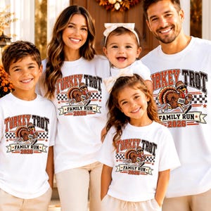 May include: A group of white t-shirts featuring a graphic of a turkey wearing a hat and sneakers, with the text Turkey Trot Family Run 2026. The design includes a checkered pattern and orange and brown lettering, displayed on a family of five.