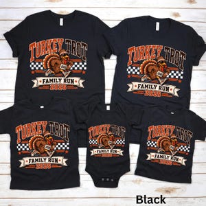 May include: A collection of five black t-shirts and one black baby bodysuit featuring a graphic of a running turkey wearing a headband and sneakers. The text reads Turkey Trot Family Run 2026 with a checkered flag pattern and orange accents.