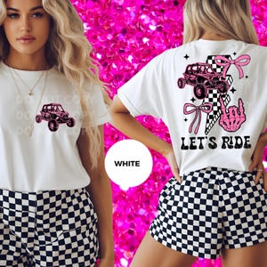 May include: White t-shirt with a pink off-road vehicle graphic on the front and back. The back design includes a checkered flag, bows, lightning bolts, and a skeleton hand. The shorts are black and white checkered.
