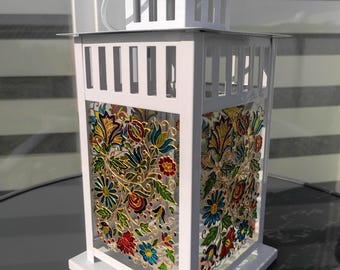 May include: White metal lantern with a floral design. The lantern features a rectangular shape with a handle and a decorative top. The glass panels are adorned with colorful flowers and leaves in red, blue, and yellow.
