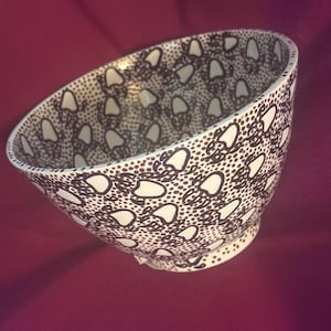 May include: White ceramic bowl with a brown dotted pattern and white teardrop shapes. The bowl has a rounded shape and a small footed base. The interior and exterior are decorated with the same pattern. The bowl is set against a burgundy background.