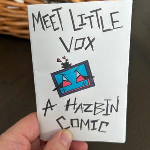 May include: A white comic book cover with the text "Meet Little Vox" and "A Hazbin Comic" in black ink. The cover features a cartoon character with a blue screen and red accents.