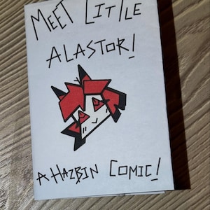 May include: A folded white paper comic book with the title "Meet Little Alastor!" in black ink. The cover features a red and black cartoon character illustration. The text "A Hazbin Comic!" is written below the illustration.
