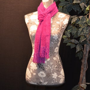 May include: A pink knitted scarf with fringe on a floral patterned mannequin.