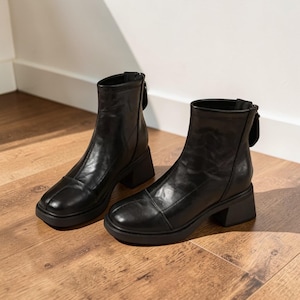 May include: A pair of black ankle boots with a square toe and a block heel. The boots have a zipper on the back and are made of a smooth leather-like material. The heels measure approximately 2 inches.