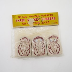 May include: A package of three monkey-shaped erasers. Each eraser depicts a monkey covering its eyes, ears, or mouth. The packaging is yellow with text that reads "NO-SEE NO-HEAR NO-SPEAK THREE MONKEY ERASERS WITH MOVING EYES".