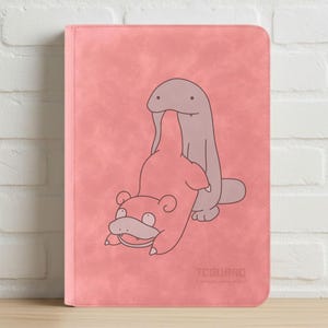 Puede incluir: Carpeta rosa con una ilustración de dibujos animados de dos personajes. Uno es una criatura rosa con forma de oso, y el otro es un personaje gris con forma de gusano. El texto "TCGUARD" está en la parte inferior.