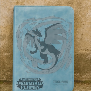 May include: A light blue card binder featuring a gray dragon design with flames. The binder has the text "MEGA EVOLUTION PHANTASMAL FLAMES" and "TCGUARD". The binder is rectangular and appears to be made of a leather-like material.