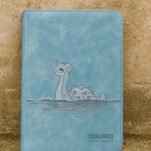 Puede incluir: Un archivador de tarjetas azul claro con una ilustración de dibujos animados de una criatura marina en el agua. El archivador tiene el texto "TCGUARD" y el lema "guard your trading cards".