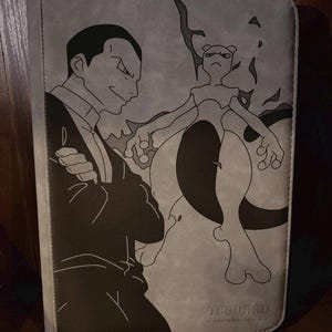 Może przedstawiać: Szary segregator na karty z czarno-białą ilustracją mężczyzny i postaci Pokémon. Segregator ma szytą obwódkę i tekst "ICEBURND" na dole.