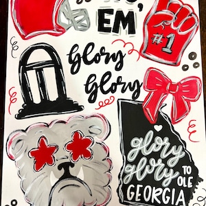 May include: A white canvas with red and black painted elements. Includes a red football helmet, a foam finger with "#1", a bulldog with red star eyes, and the words "Sic 'Em" and "Glory Glory" in black script. A red bow and the state of Georgia are also featured.
