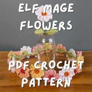 May include: A crochet flower garland with a variety of colors, including white, pink, orange, and yellow, encircles a glass vase. The text "ELF MAGE FLOWERS PDF CROCHET PATTERN" is displayed in white letters.