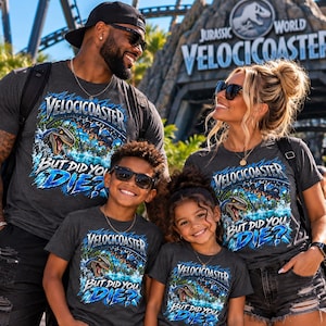 Puede incluir: Una camiseta de manga corta gris carbón con un estampado gráfico de la montaña rusa Jurassic World VelociCoaster. El diseño incluye un dinosaurio, vías de montaña rusa y el texto "VelociCoaster" sobre "But Did You Die?" en azul y blanco.