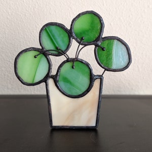 May include: A stained glass succulent plant in a white pot. The plant has five green leaves and is made of glass.