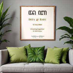 May include: A framed wedding sign with the names "DITA & BAYU" and the date "12 July 2026". The sign is in a wooden frame and has the text "Growing together in harmony". The sign is above a gray sofa with green pillows.