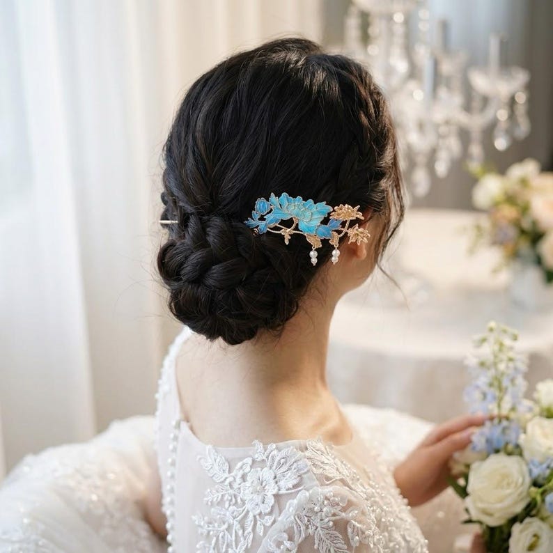 Pode incluir: Um pente de cabelo decorativo com p&eacute;talas florais azul-brilhante e ramos de metal dourado. O acess&oacute;rio &eacute; adornado com pequenas contas brancas pendentes semelhantes a p&eacute;rolas, criando um design delicado e intrincado no cabelo escuro tran&ccedil;ado.