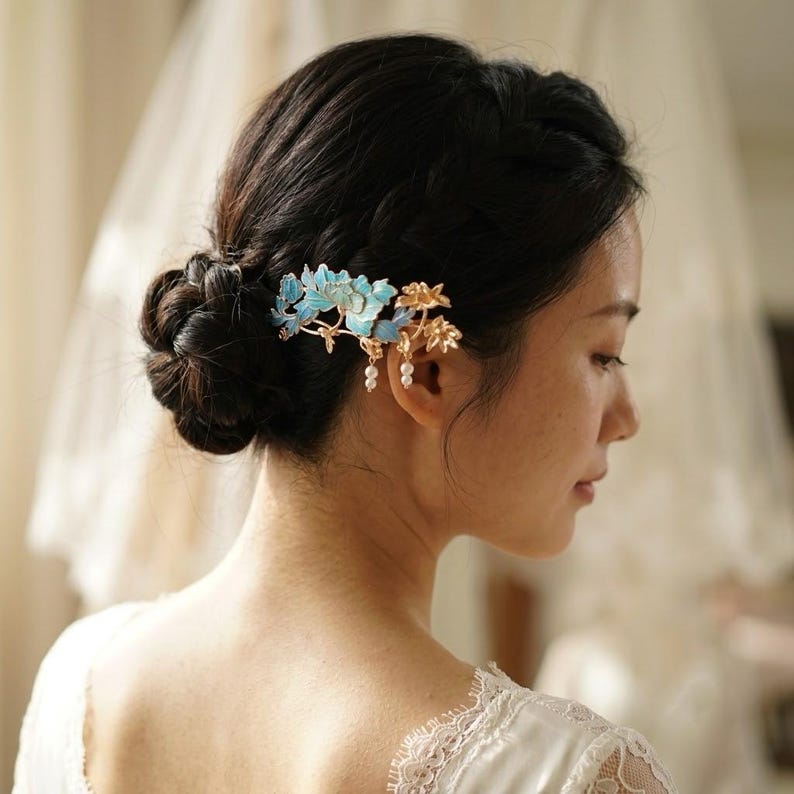 Pode incluir: Um pente de cabelo decorativo com motivos florais de metal em tons de azul turquesa e dourado. O design inclui folhas e p&eacute;talas delicadas com pequenas contas brancas semelhantes a p&eacute;rolas penduradas na base das flores de metal.