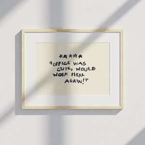 May include: A framed print with a light beige background and a wooden frame. The print features the text "OFFICE WAS CUTE, WOULD WORK HERE AGAIN!" in black, handwritten-style font, with five stars above the text.