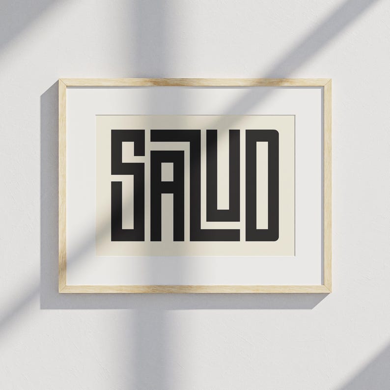 Puede incluir: Un estampado enmarcado con la palabra "SALUD" en letras geom&eacute;tricas negras y en negrita. El estampado est&aacute; sobre un fondo crema y enmarcado en un marco de madera clara. La obra de arte se exhibe en una pared blanca.