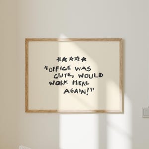 May include: A framed print with the text "OFFICE WAS CUTE, WOULD WORK HERE AGAIN!" in black handwritten font. Above the text are five black stars. The frame is a light brown color.
