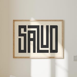 Puede incluir: Un cuadro enmarcado con la palabra "SALUD" en letras geom&eacute;tricas negras y audaces. La obra de arte est&aacute; sobre un fondo crema y encerrada en un marco de madera marr&oacute;n claro. La impresi&oacute;n se exhibe en una pared blanca.