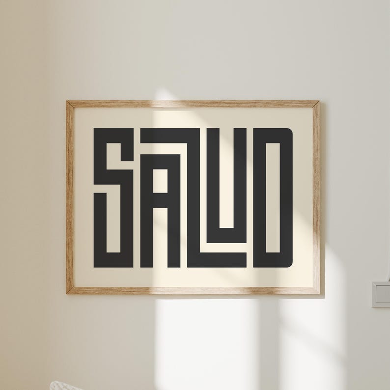 Puede incluir: Un cuadro enmarcado con la palabra "SALUD" en letras geom&eacute;tricas negras y audaces. La obra de arte est&aacute; sobre un fondo crema y encerrada en un marco de madera marr&oacute;n claro. La impresi&oacute;n se exhibe en una pared blanca.