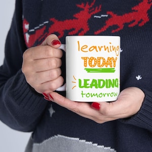 May include: A white ceramic mug featuring the colorful text "learning TODAY LEADING tomorrow" printed on the front. The word "learning" is in orange, "TODAY" is in orange with a green underline, and "LEADING tomorrow" is in bright green.
