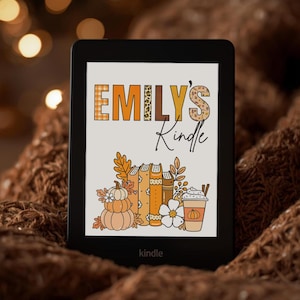 May include: A black e-reader displaying a screen with the text EMILY'S Kindle in orange, brown, and leopard print patterns. Below the text is a graphic illustration of stacked books, pumpkins, a white flower, and a coffee cup with a lid.