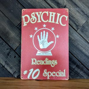 May include: A red metal sign with the word "PSYCHIC" in cream-colored letters. The sign features a white hand inside a circle, stars, and the text "Readings $10 Special". "Walk-ins Welcome" is also printed on the sign.