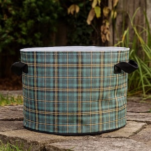 May include: A round storage container with a green, black, and yellow plaid pattern. The container has black handles and a silver-colored rim. It is sitting on a stone surface.