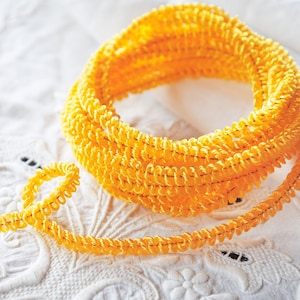 May include: A spool of bright yellow, coiled trim with a textured surface. The trim is made of a soft, flexible material and is perfect for adding a touch of color and texture to any project.