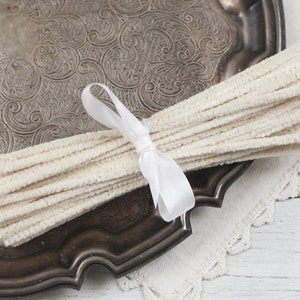 May include: A bundle of white pipe cleaners tied together with a white ribbon. The pipe cleaners are on a silver tray with an ornate design.