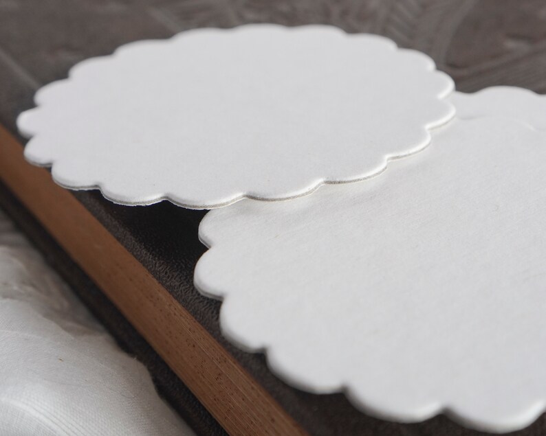 May include: Two white scalloped paper circles, stacked on top of each other, on a brown textured surface.