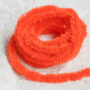 May include: A spool of bright orange fuzzy pipe cleaner. The pipe cleaner is coiled and ready to be used for crafts.