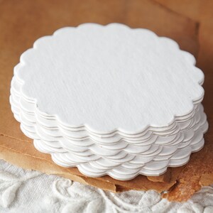 May include: A stack of white scalloped paper doilies. The doilies are round and have a delicate, lacy edge.