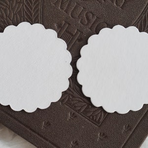May include: Two white scalloped paper circles on a brown textured surface.