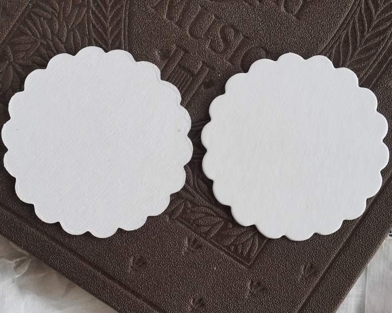 May include: Two white scalloped paper circles on a brown textured surface.