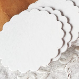 May include: A stack of white scalloped paper doilies. The doilies are made of thin, delicate paper and have a scalloped edge.
