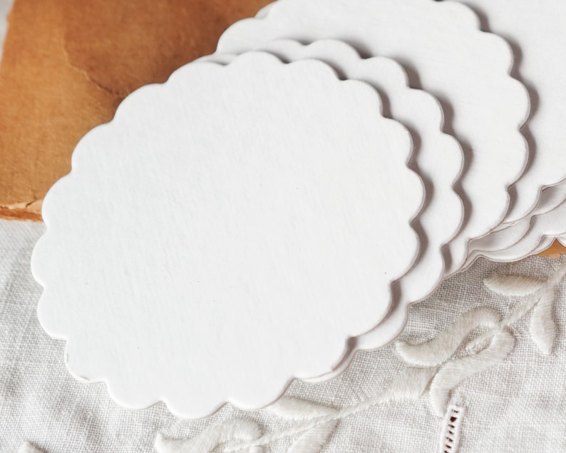 May include: A stack of white scalloped paper doilies. The doilies are made of thin, delicate paper and have a scalloped edge.