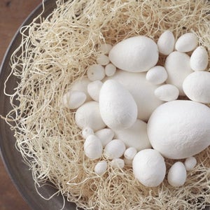 May include: A bowl filled with white, round, decorative eggs nestled in a bed of beige, wispy straw.