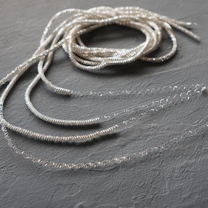 Puede incluir: Una guirnalda metálica plateada con un diseño en espiral. La guirnalda está hecha de varios hilos de alambre que se retuercen juntos para crear un efecto decorativo.